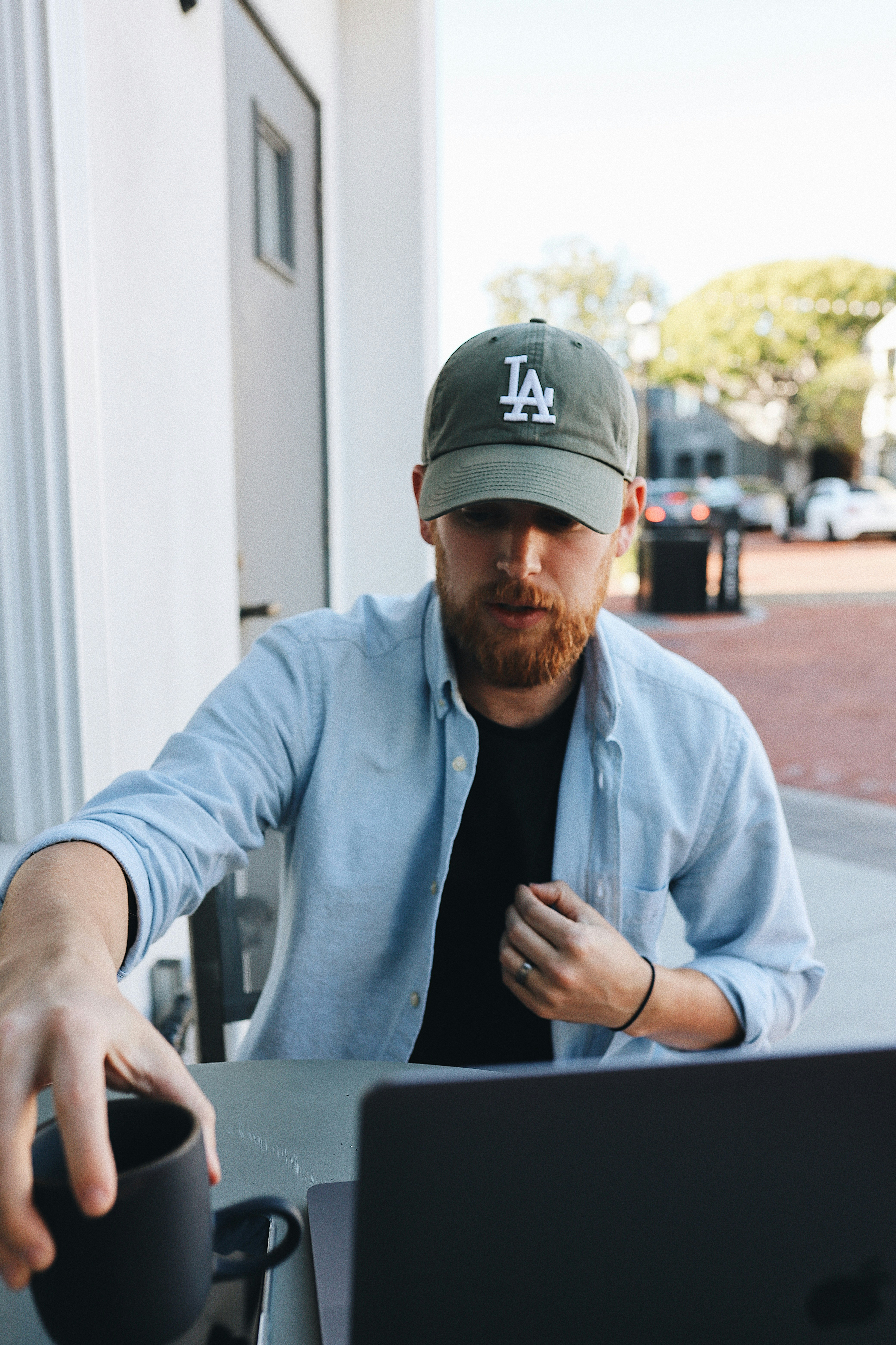 man in gray dress shirt and black cap sitting by the table